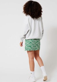 Felpa grigia e mini gonna a motivi floreali verdi, con sneakers e calze bianche. Presenta una silhouette rilassata e colori vivaci.