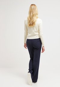 Top de manga larga crema combinado con pantalones a medida azul marino, con corte recto y bolsillos traseros, llevado con zapatillas blancas.