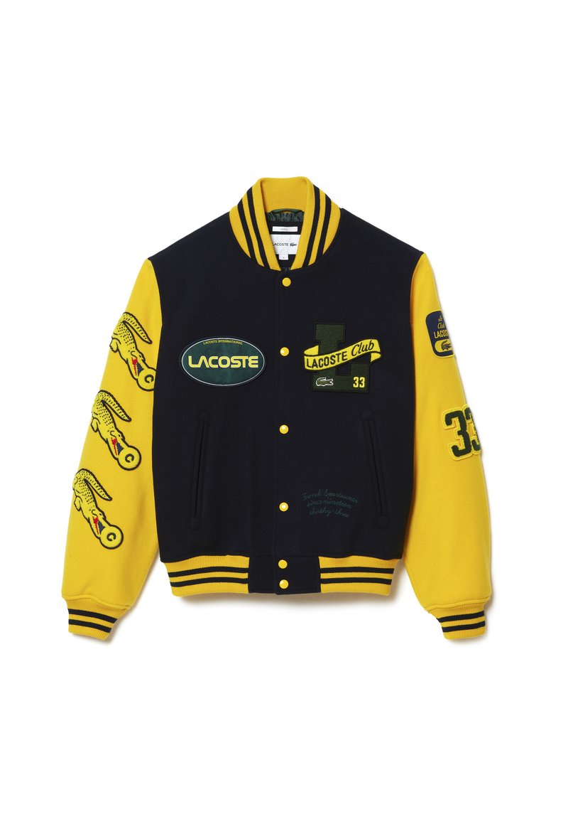 Veste varsity Lacoste en noir et jaune, dotée de patchs brodés, de poignets contrastés et d'un col côtelé. Présentée de face.