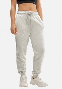 Pantalones de chándal de algodón gris claro con cintura elástica, detalle de cordón, bolsillos laterales y tobillos ajustados, combinados con zapatillas blancas.