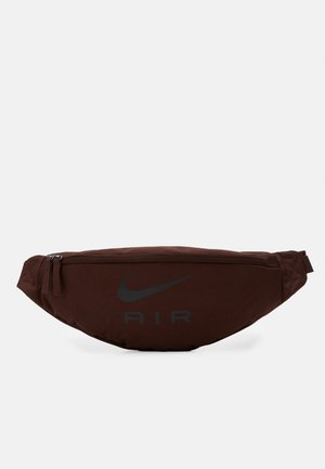 Tummanruskea Nike Air -vyölaukku, jossa kaksi vetoketjua ja säädettävä hihna, esillä yksinkertaista valkoista taustaa vasten.