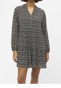 Robe florale noire avec un décolleté en V, des manches longues et transparentes, et une silhouette fluide. Présente de petits motifs de fleurs blanches et roses partout.