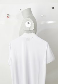 White FILA polo shirt hanging on a gray mannequin torso with hooks on a white wall background.