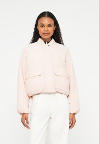 Veste bomber rose clair avec un col rond, deux poches avant et des poignets élastiques. Fabriquée en tissu léger, avec un design court.