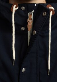 Marinblå huvjacka tillverkad av slitstarkt material. Har en framdragkedja med läderdrag och bomullssnören, silverfärgade tryckknappar och fickor.