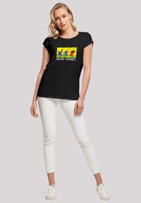 Black t-shirt featuring colorful superhero graphic with text "SUPER HEROES" on a rectangular yellow background. Soft material, relaxed fit.