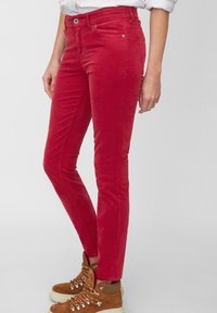 Rode corduroy broek met een slim fit, voorzien van een flat front, achterzakken en een knoopsluiting. Gemaakt met bruine veterschoenen.