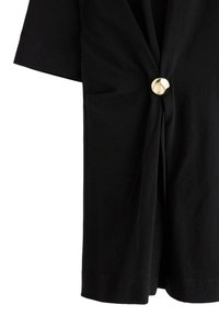 Blusa nera a maniche corte, con design frontale annodato, dettaglio di bottoni dorati e tasca laterale. Tessuto dalla texture liscia.