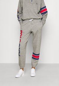 Grå fleecebyxor med elastiska mudd, med "Polo" tryckt i röd och blå. I kombination med en matchande grå zip-up-tröja och vita sneakers.