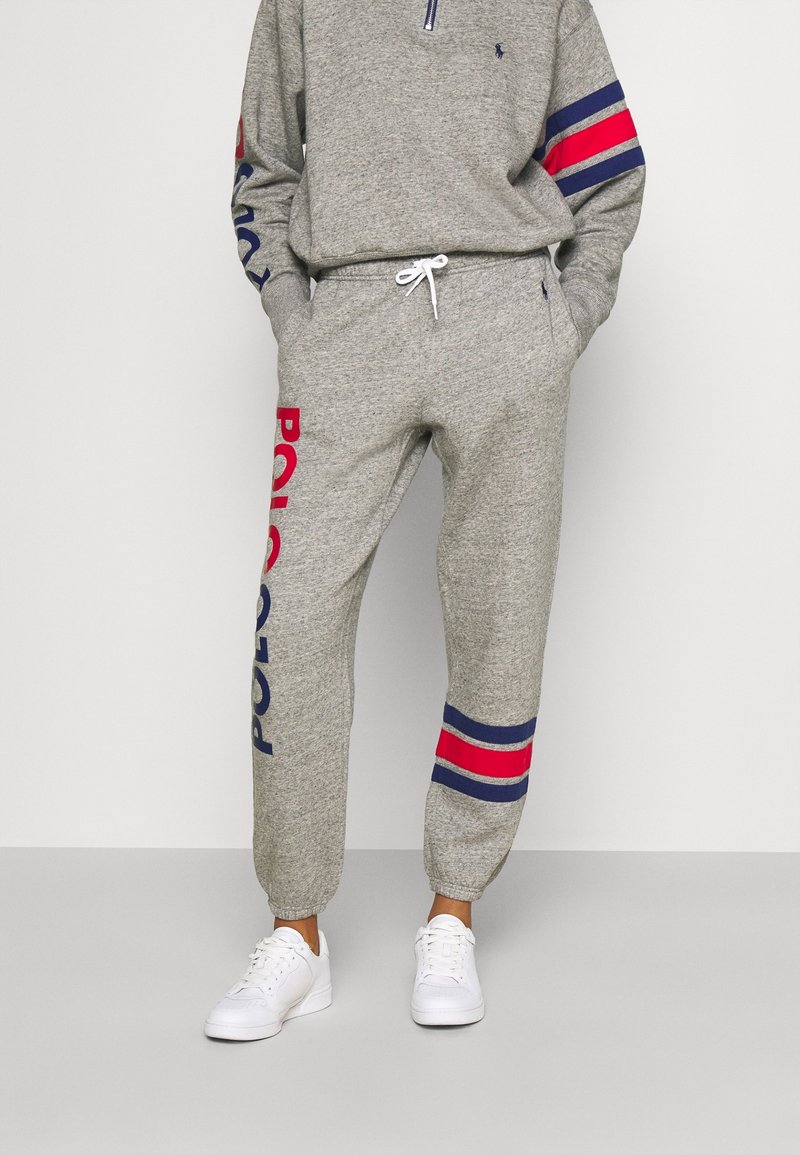 Grå fleecebyxor med elastiska mudd, med "Polo" tryckt i röd och blå. I kombination med en matchande grå zip-up-tröja och vita sneakers.