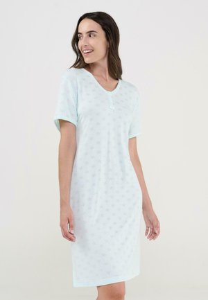 Mujer vestida con un vestido azul claro hasta la rodilla, de manga corta y con un sutil patrón de estrellas, sonriendo y mirando hacia un lado.