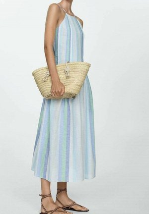 Femme portant une robe midi sans manches à rayures, tenant un sac en paille tressée, assortie à des sandales plates marron à brides.