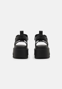 Black leather platform sandals featuring wide straps, a buckle accent, and a textured sole. The design offers an open-back style.