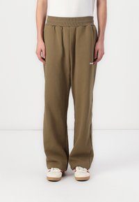 Olivgrüne Sweatpants mit elastischem Bund, lockerer Passform, seitlichen Taschen und einem kleinen weißen Logo am linken Oberschenkel. Einfache Textur.