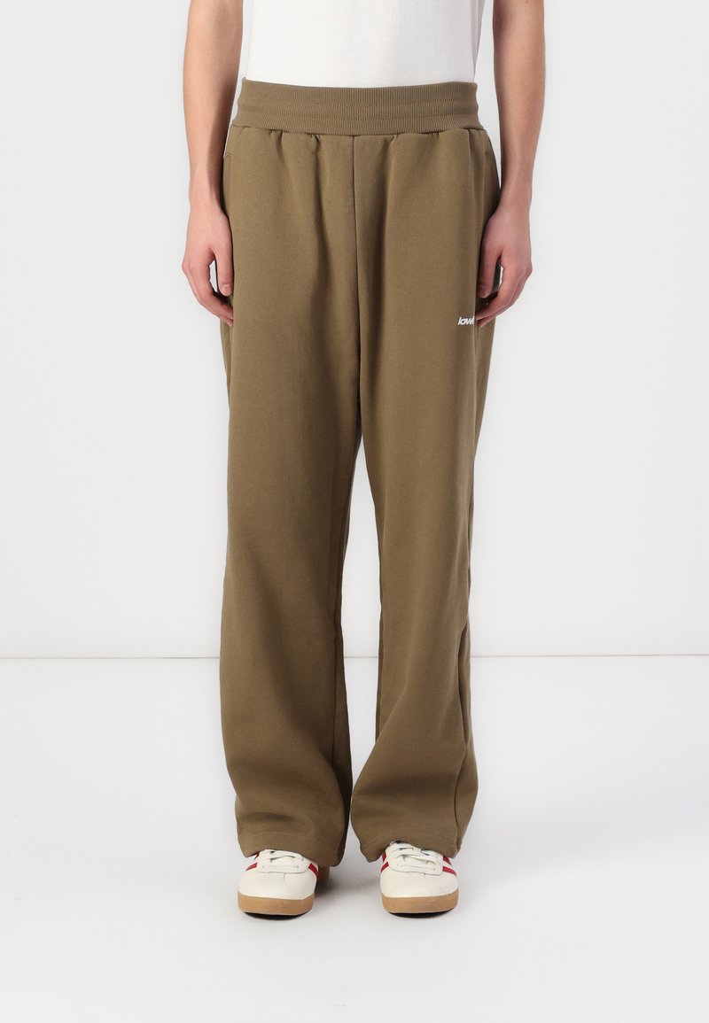Olivgrüne Sweatpants mit elastischem Bund, lockerer Passform, seitlichen Taschen und einem kleinen weißen Logo am linken Oberschenkel. Einfache Textur.