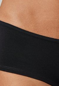 Zwarte stoffen slip met een gladde textuur en een brede tailleband. Close-upweergave van de stikdetails en de huidtint langs de rand.