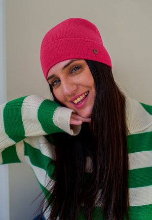 Pink knit beanie with a ribbed texture and a small logo, paired with a green and white striped sweater, featuring a relaxed fit.