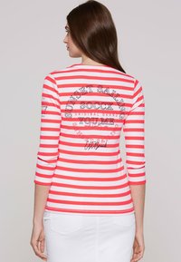 Red and white striped long-sleeve top with ribbed texture, featuring a graphic print on the back that includes text and brand details.