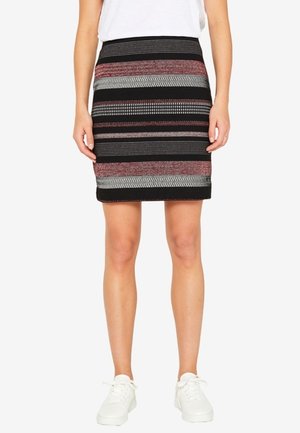 Černá pruhovaná sukně s vodorovnými pásy v červené, bílé a šedé barvě; pletená textura; délka nad kolena; nošena s bílými teniskami.