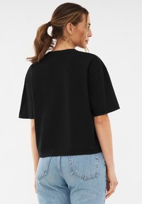 Camiseta negra recortada con mangas cortas, ajustada de forma relajada, hecha de algodón suave. Presenta un cuello redondo y un diseño minimalista sin adornos.