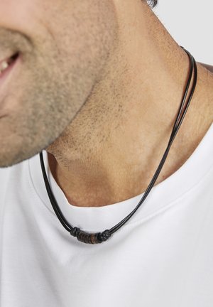 Leder-Multi-Strang-Halskette mit dunkelbraunen und hellbraunen Perlen, auf einem weißen Hemd liegend vor hellem Hintergrund.