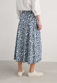 Sati kukkakuosisia, nilkkapituinen hame tummansinisessä ja valkoisessa, jossa on poimuja ja korkea vyötärö. Yhdistetty neutraalinsävyisiin kangaskenkiin.