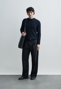 Juodas ribuotas megztinis, laisvo kirpimo juodos kelnės ir derančios plokščios bateliai. Ant peties nešiojama juoda odinė rankinė.