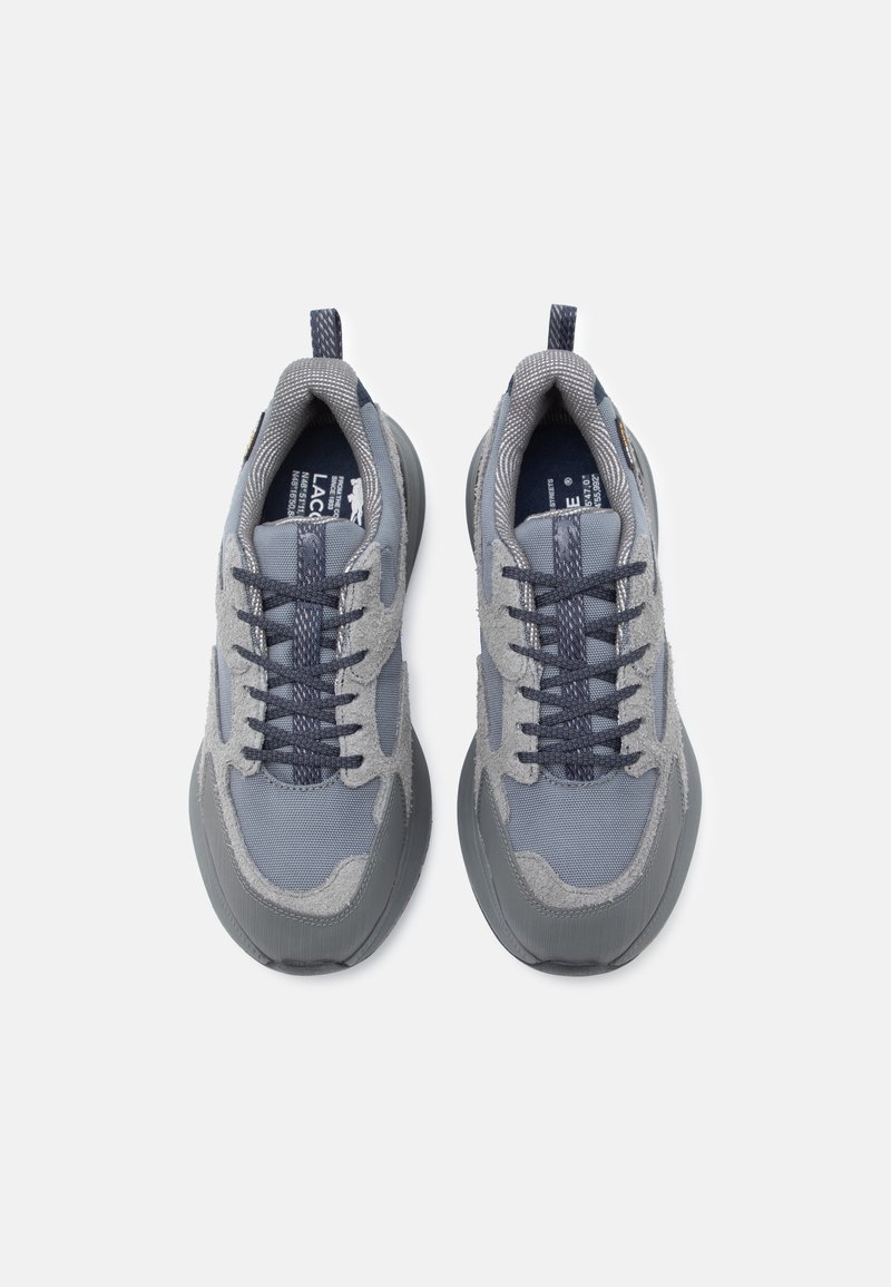 Graue Sportschuhe mit strukturiertem Mesh und Wildlederpaneelen, ausgestattet mit dunkelgrauen Sohlen und Schnürsenkeln sowie einer Ziehlasche an der Ferse.