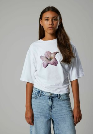 T-shirt bianco con una grande grafica di un giglio rosa, vestibilità rilassata, scollo a girocollo, abbinato a jeans in denim azzurro, che mostra un design casual.