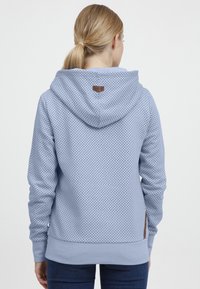 Felpa azzurra chiara con piccoli pois neri, dotata di cappuccio con cordino e tessuto texturizzato. Accent logo marrone vicino al colletto.