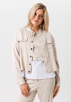Veste beige courte avec des boutons-pression, deux poches poitrine et un col mandarin. Tissu léger avec une texture lisse.