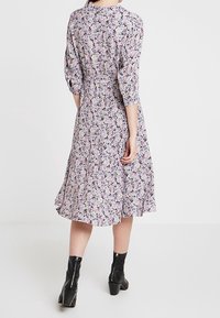 Blommig midiklänning i ljuslila, med trekvartsärmar, en figurnära midja och en utsvängd nederkant, kombinerad med svarta ankelkängor.