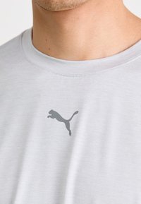 Světle šedé tričko vyrobené z měkké látky, s malým tmavě šedým logem Puma na prsou. Kl klasikický design s kruhovým výstřihem.