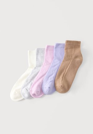 Cinq paires de chaussettes chevilles côtelées en blanc, gris clair, rose, lavande et beige, posées côte à côte sur un fond clair.