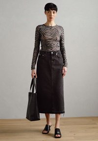 Langärmliges, gestreiftes Sheer-Oberteil mit rundem Ausschnitt, kombiniert mit einem hoch taillierten schwarzen Jeansrock und schwarzen Slidesandalen; trägt eine Tote-Tasche.