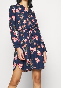 Blumenmuster-Kleid in Marineblau mit rosa und pfirsichfarbenen Blumenprints, Knopfverschluss, langen Ärmeln und verstellbarem Bindegürtel. Weicher, leichtes Material.