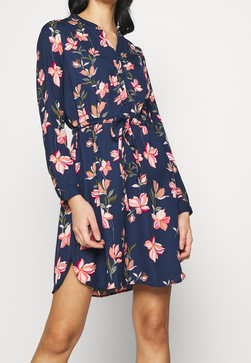 Blumenmuster-Kleid in Marineblau mit rosa und pfirsichfarbenen Blumenprints, Knopfverschluss, langen Ärmeln und verstellbarem Bindegürtel. Weicher, leichtes Material.