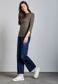 Olivegrünes, geripptes Langarmoberteil kombiniert mit dunkelblauen, weit geschnittenen Jeans und weißen Sneakern mit beigen Akzenten. Einfaches, figurbetontes Design mit weicher Textur.