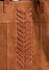 Sac fourre-tout en daim marron avec un design en chevrons réalisé en bandes de cuir sur le devant, doté de poignées solides en marron et de détails de couture.