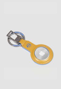 Portachiavi in pelle gialla con accenti blu, anello argentato e una sezione circolare trasparente che mostra il logo Apple.