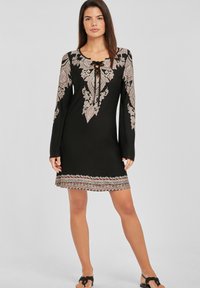 Vestido negro con intrincado bordado floral en rosa y blanco, mangas largas, escote en forma de barco con detalle de cordones y patrón decorativo en el dobladillo.