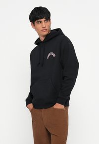 Sort hættetrøje lavet af bomuldsblanding, med en frontlomme og snor i hætten. Lyserød buet tekst "TOMMY JEANS" på brystet. Casual pasform.
