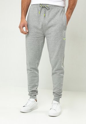 Pantalones deportivos grises hechos de un tejido suave, con un cordón de ajuste con acentos amarillos, puños elásticos, dos bolsillos laterales y un detalle de logo sutil.