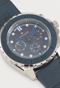 Reloj de hombre con una correa de silicona azul oscura, caja de acero inoxidable plateado y una esfera gris que presenta acentos blancos y azules, funciones de cronógrafo y una pantalla de fecha.