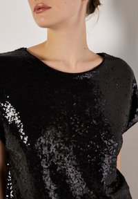 Zwarte pailletten top met korte mouwen, ronde halslijn en een glanzende textuur, met een volledig paillettenpatroon voor een reflecterend effect.