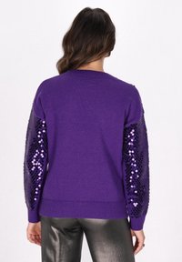 Pulover violet cu manșete embellishate cu paiete, textură tricotată și tiv cu nervuri. Manșetele au un design lucios, cu paiete modelate.