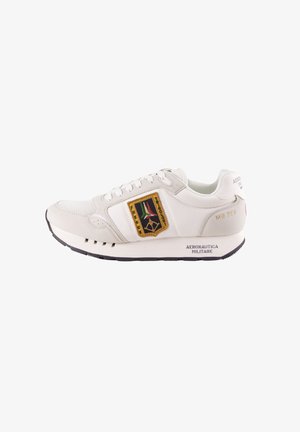 Sneakers bianchi con un design in mesh e pelle, un emblema giallo e nero ben visibile, e suole in gomma nera con dettagli di branding.