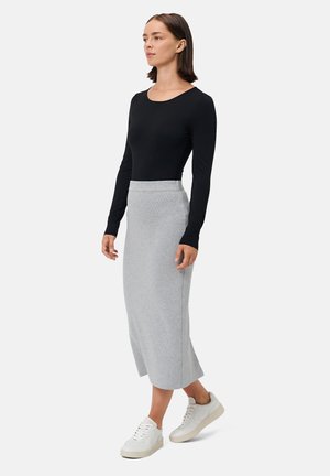 Czarna bluzka z długim rękawem zestawiona z szarym, mięsistym wzoru do kolan, noszona z białymi trampkami z teksturowaną podeszwą.