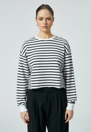 Gestreifter, kurzer Sweatshirt in Weiß und Schwarz, mit langen Ärmeln, runder Ausschnitt und rohem Saum. Kombiniert mit maßgeschneiderten schwarzen Hosen.