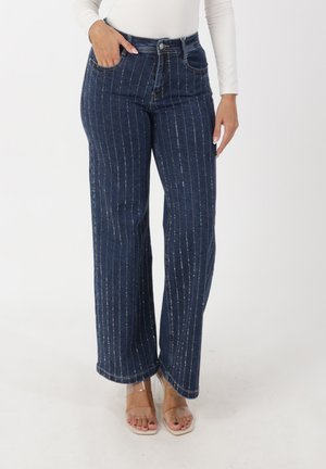 Jean en denim foncé à jambes larges avec des rayures argentées verticales, une taille haute, des poches avant et un ourlet légèrement effiloché.